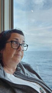 a woman sitting by a cruisehip window looking out onto the ocean.