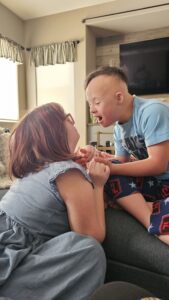Ben leans toward his sister with a joyful expression as they hold hands and connect face-to-face on the couch.