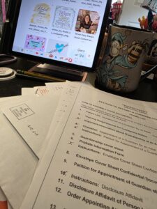 Caregiving paperwork and forms are spread across a desk beside a tablet, pencils, and an Eeyore mug, showing the everyday administrative side of family life.