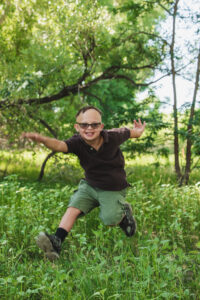 Ben runs joyfully through a green wooded area with his arms outstretched and a big smile on his face.
