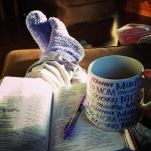 Open Bible with a purple pen and a large “Mama” coffee mug resting beside cozy sock-covered feet in the morning light.