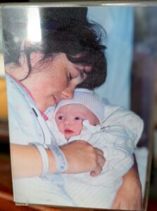A younger Cindy rests beside her newborn baby, holding the baby close while wearing a hospital wristband.